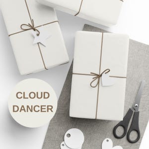 May include: Three white wrapped gift boxes tied with brown twine and adorned with white paper tags. A pair of black handled scissors and additional tags are on a gray cloth. The text "CLOUD DANCER" is in a circle.