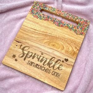 Puede incluir: Una tabla de cortar de madera con un borde de chispas de colores. La tabla está grabada con el texto "Sprinkle Sandwiches Only".