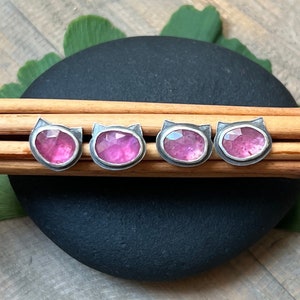 Puede incluir: Cuatro pendientes de plata en forma de gato con piedras preciosas rosas engastadas en el centro.