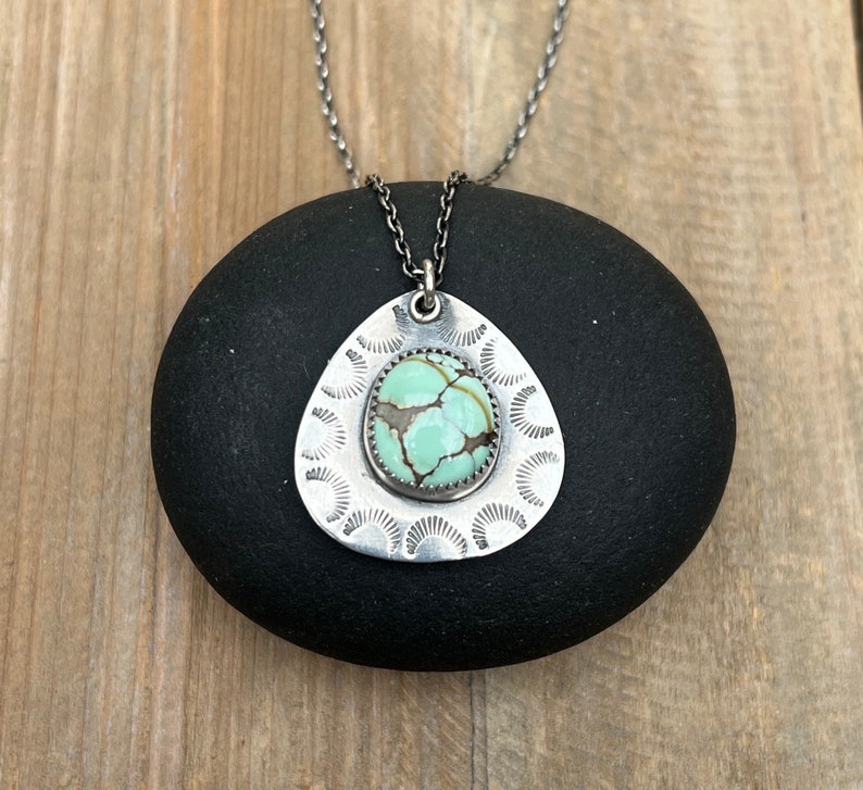 May include: A silver necklace with a turquoise stone pendant. The pendant is shaped like a teardrop and has a decorative design around the edge.