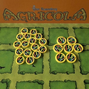 May include: A close-up of a game board with yellow and green squares. There are two sets of round tokens, one set with the number "1" and the other with the number "5".