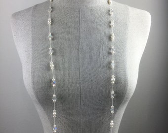 Pode incluir: Um colar longo e delicado com contas de cristal transparente e pérolas brancas alternadas. O colar é exibido em um manequim branco.