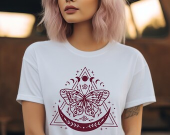 May include: White t-shirt with a burgundy butterfly graphic design. The butterfly is surrounded by a crescent moon, stars, and a triangle.