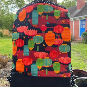 May include: Black fabric with a red, green, and orange pattern of Chinese lanterns and lotus flowers. The fabric is on a black mannequin.