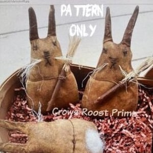 Peut inclure: Deux poupées de lapin en tissu brun avec de longues oreilles et un bâton dans les mains. Les lapins sont assis dans un panier rempli de papier déchiqueté. Le texte "PATTERN ONLY" est écrit en lettres blanches sur fond noir au-dessus des lapins.