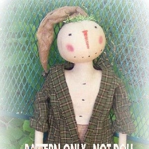 May include: A pattern for a rag doll with a plaid shirt and brown shorts. The doll has a round face with a stitched-on nose and rosy cheeks. The text "PATTERN ONLY - NOT DOLL" is visible in the image.