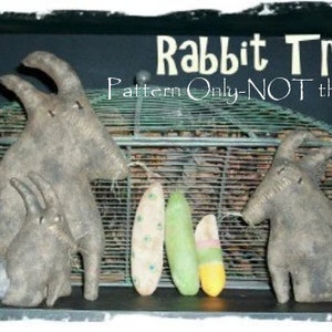 May include: A pattern for making three primitive style fabric rabbits. The pattern is called "Rabbit Trio" and the text "Pattern Only-NOT the doll" is also visible in the image.