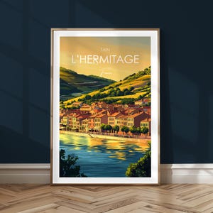 Könnte beinhalten: Ein Vintage-Reiseposter mit einer farbenfrohen Illustration einer Stadt namens "L'Hermitage" in Tain, Frankreich. Das Poster zeigt eine malerische Stadt mit Gebäuden, die einen Fluss säumen, umgeben von sanften Hügeln.