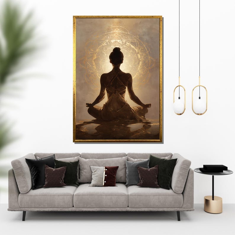 May include: A framed artwork depicts a person in a meditative pose, set against a golden, circular backdrop. The artwork is in a gold frame and hangs above a gray sofa with decorative pillows. Two pendant lights hang from the ceiling.
