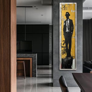 May include: A black and white illustration of a person wearing a hat and suit standing on a yellow and black background. The artwork is framed and hanging on a wall in a modern interior.