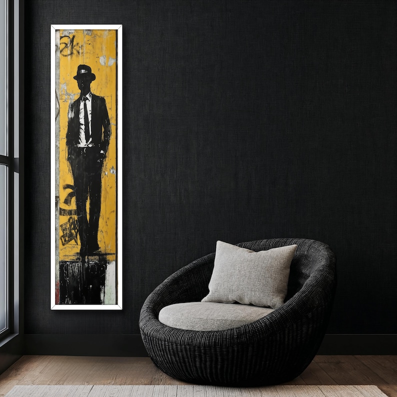 May include: A black and white silhouette of a person wearing a hat and suit standing in front of a yellow and white background. The image is framed and hanging on a black wall next to a gray wicker chair with a gray cushion.
