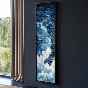 Puede incluir: Una pintura vertical de un océano azul con olas blancas rompiendo. La pintura está enmarcada en negro y está colgada en una pared gris oscuro.