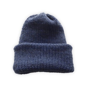 May include: A navy blue knit beanie hat with a folded brim. The hat is made of a thick, textured yarn and is designed to keep the head warm. The hat is a solid color and is suitable for cold weather.