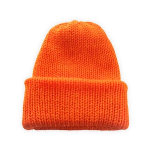 Könnte beinhalten: Leuchtend orangefarbene Strickmütze. Die Mütze besteht aus dickem, strukturiertem Garn und hat einen umgeschlagenen Saum. Die Mütze ist einfarbig und leuchtend orange.