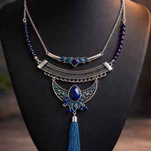 May include: A two-strand necklace with silver-tone metal and blue accents. The top strand has small blue beads and a bar with blue gems. The lower strand features a large blue pendant with a tassel.