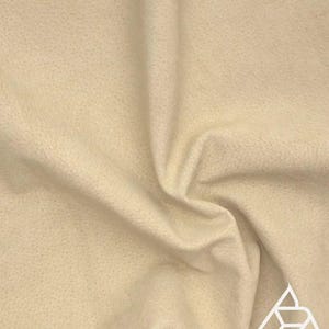 May include: A close-up of a cream-colored fabric with a textured surface. The fabric is soft and smooth, and it has a subtle sheen.