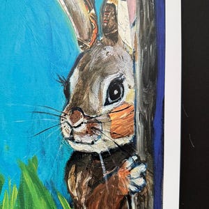 Op de afbeelding: Een schilderij van een bruin en wit konijn dat achter een boom vandaan gluurt. Het konijn heeft lange oren met gedetailleerde patronen. De achtergrond is blauw met groen gras.