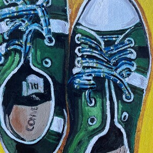 May include: A pair of green canvas sneakers with white laces and white trim. The laces are tied in a criss-cross pattern and the shoes are sitting on a yellow background.