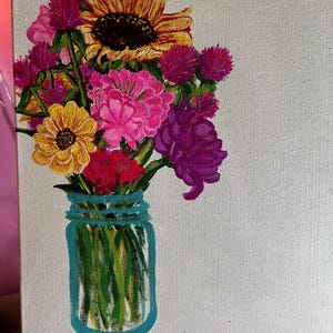 May include: A painting of a bouquet of flowers in a blue mason jar. The flowers include a sunflower, pink carnations, purple and pink wildflowers, and yellow flowers. The background is a light green canvas.