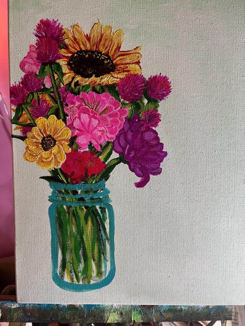May include: A painting of a bouquet of flowers in a blue mason jar. The flowers include a sunflower, pink carnations, purple and pink wildflowers, and yellow flowers. The background is a light green canvas.
