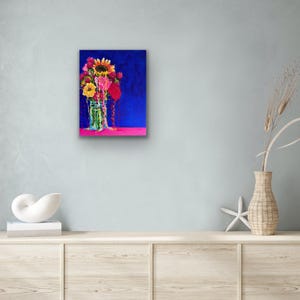 May include: A painting of a bouquet of sunflowers, pink and yellow flowers in a clear glass jar on a pink surface against a blue background.