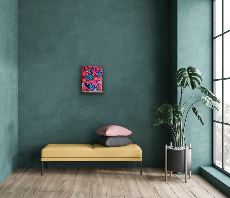 May include: A framed abstract painting with a vibrant mix of red, pink, and blue flowers on a dark blue background. The painting is hanging on a teal wall in a modern living room setting.