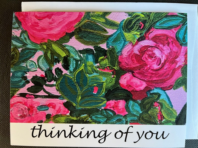 May include: A pink and green floral greeting card with the text "thinking of you" in black cursive writing.
