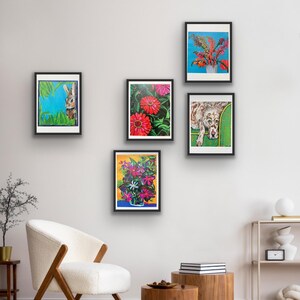 Op de afbeelding: Vijf ingelijste kunstdrukken tentoongesteld op een witte muur. De prints tonen kleurrijke bloemstukken, een konijn en een hond. De frames zijn zwart en de kunstwerken hebben levendige kleuren. De kamer bevat een witte stoel en houten bijzettafels.