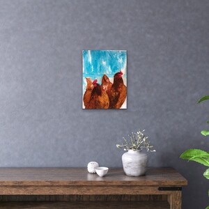 Op de afbeelding: Een schilderij van drie bruine kippen met rode kammen die voor een blauwe en witte achtergrond staan.