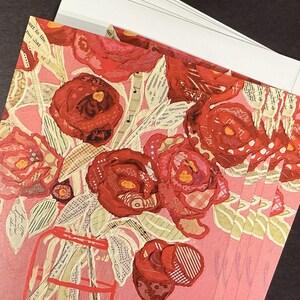 May include: A stack of greeting cards featuring a collage of red roses in a vase. The roses are made from various patterned fabrics and paper, set against a pink background. White envelopes are visible.