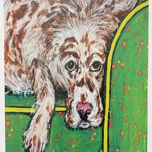 May include: An acrylic painting of a brown and white spotted dog with a pink nose resting on a green sofa with a yellow trim and a small orange floral pattern. The artwork features visible brushstrokes and the signature Susannah in the bottom corner.