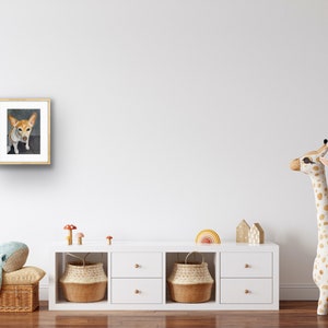 May include: A framed watercolor painting of a small, white and brown dog with brown ears. The dog is looking directly at the viewer. The painting is hanging on a white wall in a room with a white dresser and a stuffed giraffe.