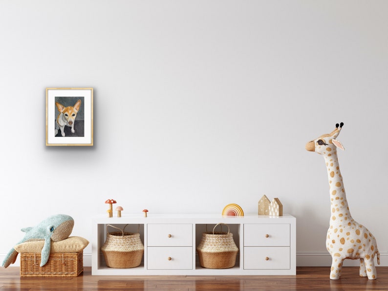 May include: A framed watercolor painting of a small, white and brown dog with brown ears. The dog is looking directly at the viewer. The painting is hanging on a white wall in a room with a white dresser and a stuffed giraffe.