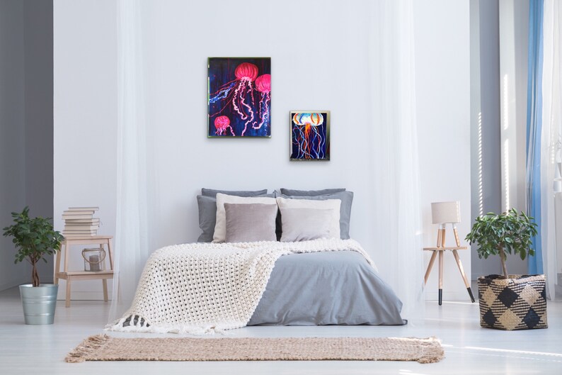 May include: Two framed paintings of jellyfish in a bedroom setting. The larger painting features three pink jellyfish with long tentacles against a dark blue background. The smaller painting features one jellyfish with a white and blue body and long tentacles against a dark blue background.