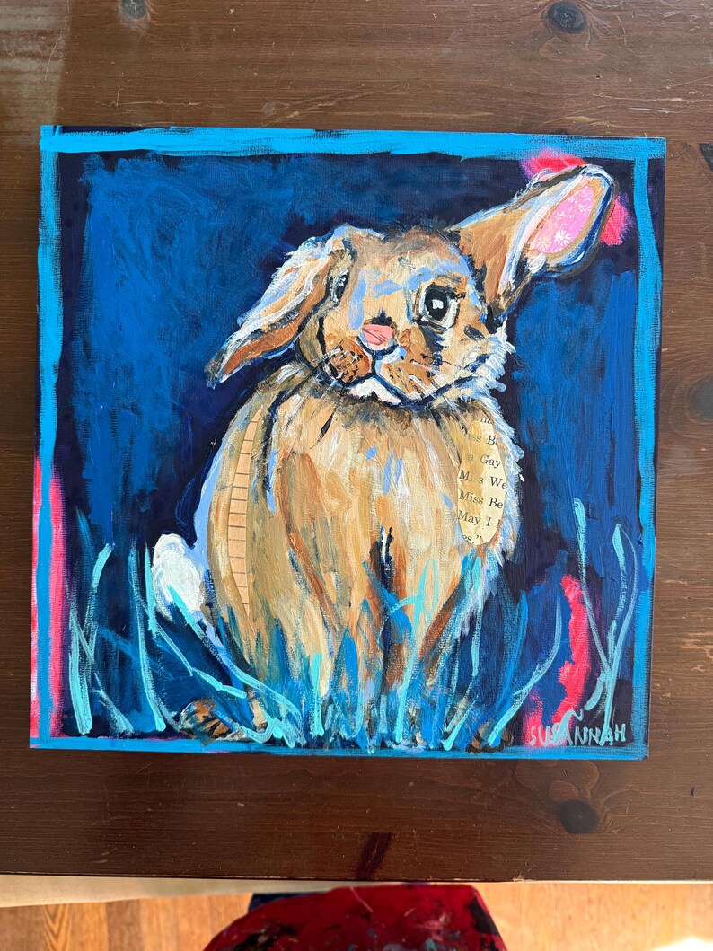 May include: A square painting of a brown rabbit with long ears, set against a deep blue background. The rabbit is painted with textured brushstrokes, and the ears have pink accents. The artwork includes blue and pink vertical strokes and the artist's signature.