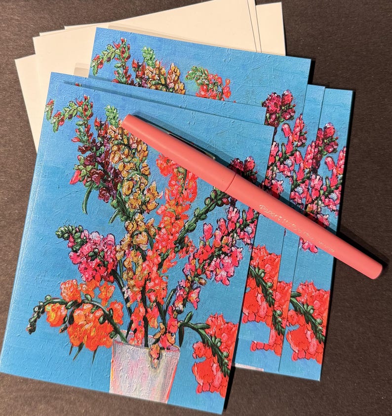 Peut inclure: Un ensemble de cartes de v&oelig;ux florales avec un fond bleu clair et un stylo rose. Les cartes pr&eacute;sentent une peinture color&eacute;e de fleurs dans un vase. Des enveloppes blanches sont empil&eacute;es en arri&egrave;re-plan.