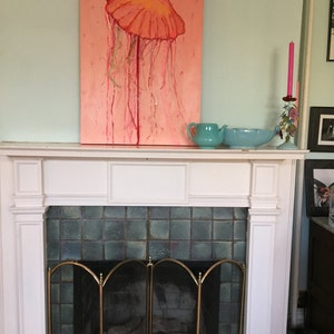 May include: A painting of a pink jellyfish with a yellow bell hanging above a white fireplace with a green tile surround and a brass screen.