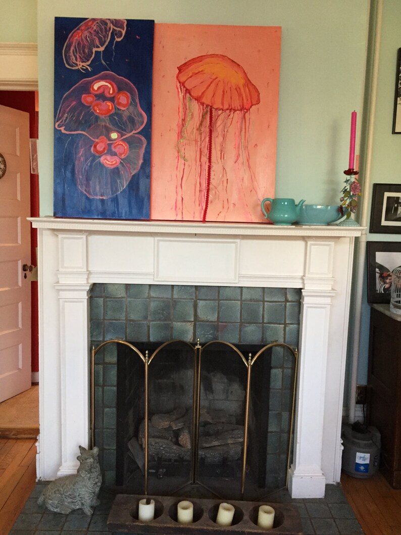 May include: Two paintings of jellyfish, one with a blue background and a pink jellyfish, the other with a pink background and a red jellyfish. The paintings are hanging above a white fireplace with a black grate.
