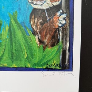 Op de afbeelding: Origineel schilderij van een konijn dat achter een boom vandaan gluurt. Het kunstwerk toont een helderblauwe lucht, groen gras en een bruin-wit konijn. De handtekening van de kunstenaar is rechtsonder zichtbaar.