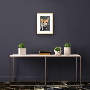 May include: A framed watercolor painting of a small, white and brown dog with floppy ears, looking directly at the viewer. The dog is sitting on a gray background. The frame is a light wood color.