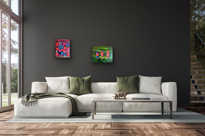 May include: Two paintings hanging on a dark gray wall above a white couch. The painting on the left features a colorful floral pattern. The painting on the right shows three people walking in a green field.