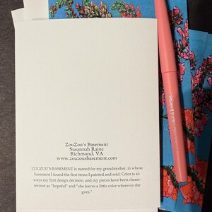 Peut inclure: Un ensemble de cartes blanches avec un stylo rose et des cartes d'art floral. Les cartes d'art floral ont un fond bleu avec des fleurs rouges et vertes. Le texte sur la carte indique "ZouZou's Basement" et l'adresse du site web.