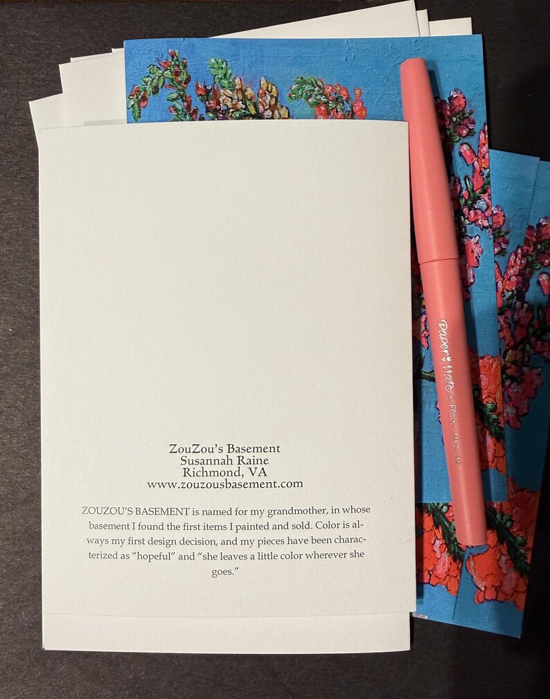 Peut inclure: Un ensemble de cartes blanches avec un stylo rose et des cartes d'art floral. Les cartes d'art floral ont un fond bleu avec des fleurs rouges et vertes. Le texte sur la carte indique "ZouZou's Basement" et l'adresse du site web.