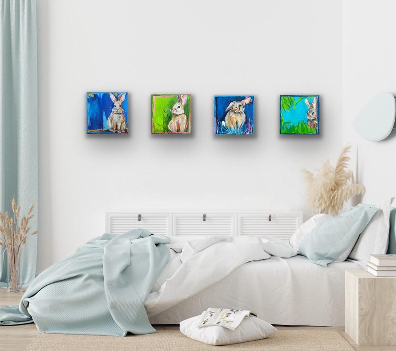 Peut inclure: Quatre peintures carr&eacute;es de lapins dans diverses poses. Chaque peinture pr&eacute;sente un lapin diff&eacute;rent sur un fond color&eacute;. Les peintures sont expos&eacute;es au-dessus d'un lit avec une couverture bleu clair.