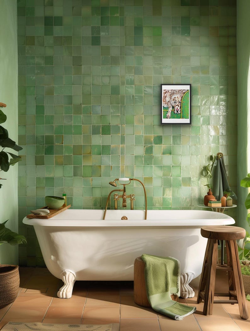 May include: A framed rectangular wall art print featuring a spotted dog resting on a green sofa, displayed on a wall covered in square light green tiles above a white clawfoot bathtub with brass fixtures and a wooden stool with a green towel.