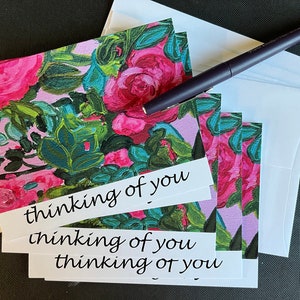 May include: A stack of pink floral note cards with white envelopes. The cards have the text "thinking of you" written on them.