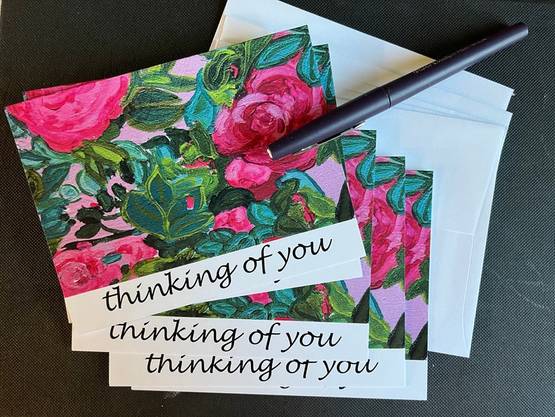 May include: A stack of pink floral note cards with white envelopes. The cards have the text "thinking of you" written on them.