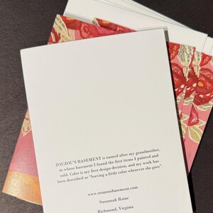 May include: A stack of white cards with a floral design on the edges, and a white card in front with text. The text on the card reads "ZOUZOU'S BASEMENT" and includes a website and the name "Susannah Raine" and the city "Richmond, Virginia."