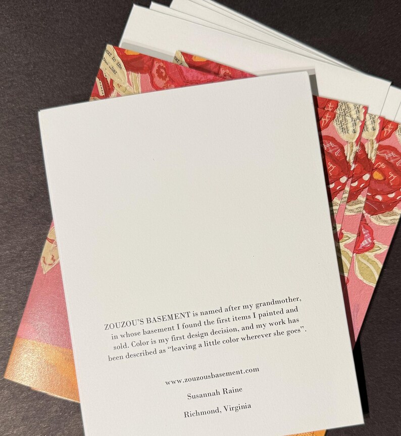 May include: A stack of white cards with a floral design on the edges, and a white card in front with text. The text on the card reads "ZOUZOU'S BASEMENT" and includes a website and the name "Susannah Raine" and the city "Richmond, Virginia."
