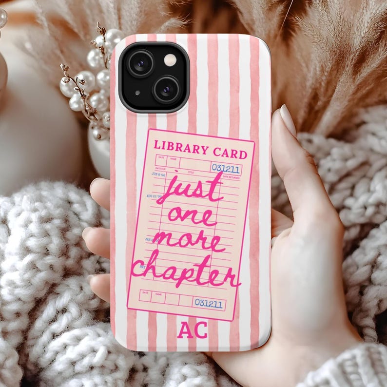 Puede incluir: Funda de tel&eacute;fono con rayas rosas y blancas. La funda presenta un dise&ntilde;o de tarjeta de biblioteca rosa con el texto "just one more chapter" en cursiva. Las iniciales "AC" est&aacute;n en la parte inferior.